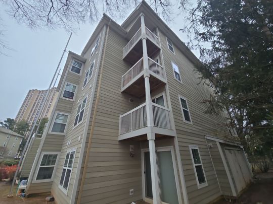 A multi-storey residential apartment building with tan vertical siding and white-railed balconies, photographed from close range at a low angle on an overcast day.
